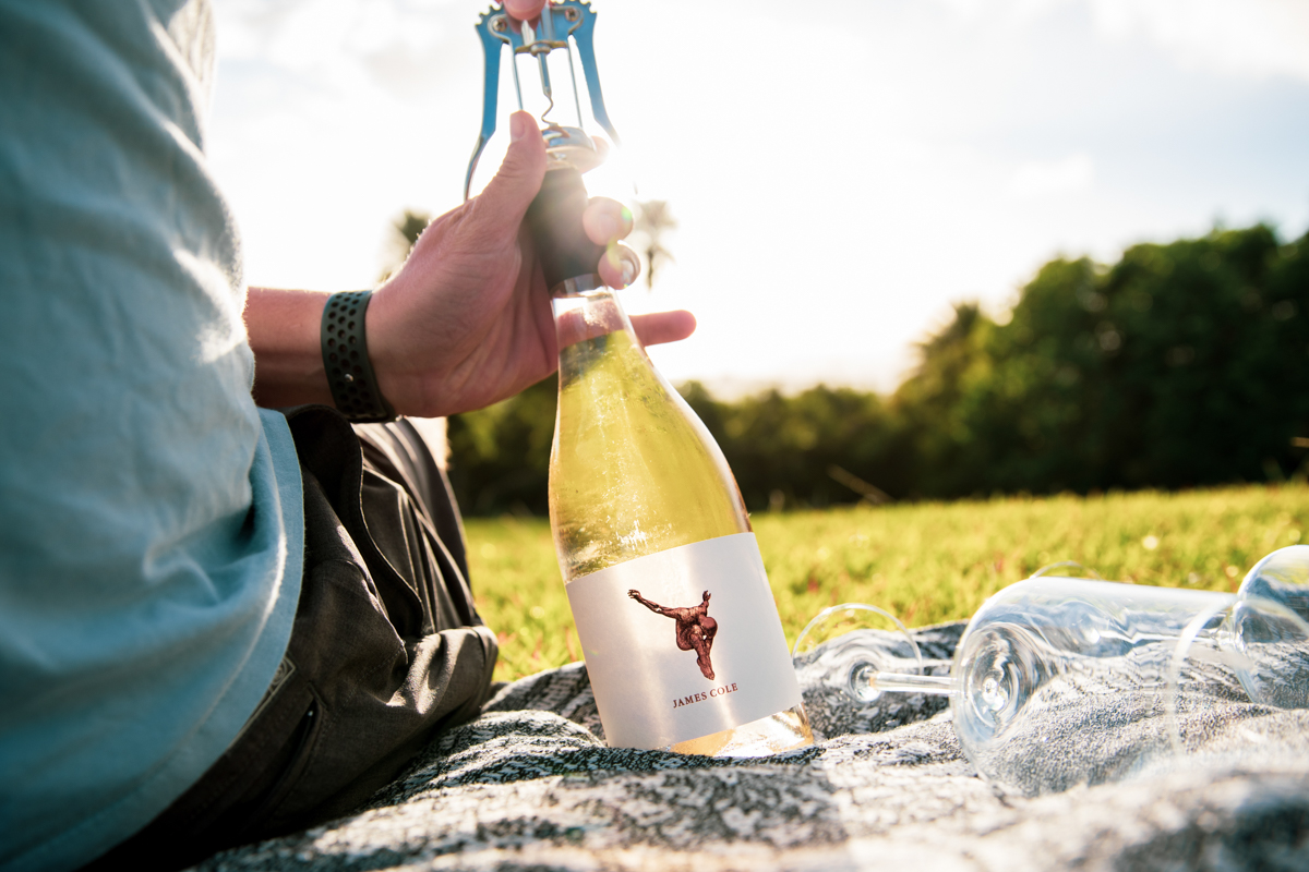 A person opening Rosé on a blanket during summer.