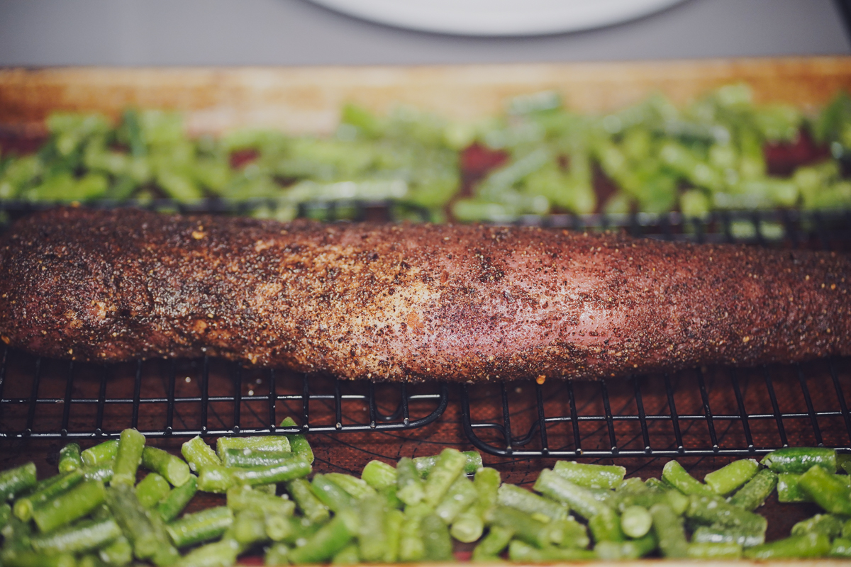 Pork tenderloin with coffee rub surrounded by green beans before it goes into the oven.