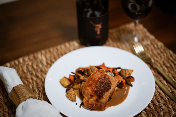 A roast chicken thigh plated with roasted vegetables and a pan sauce.