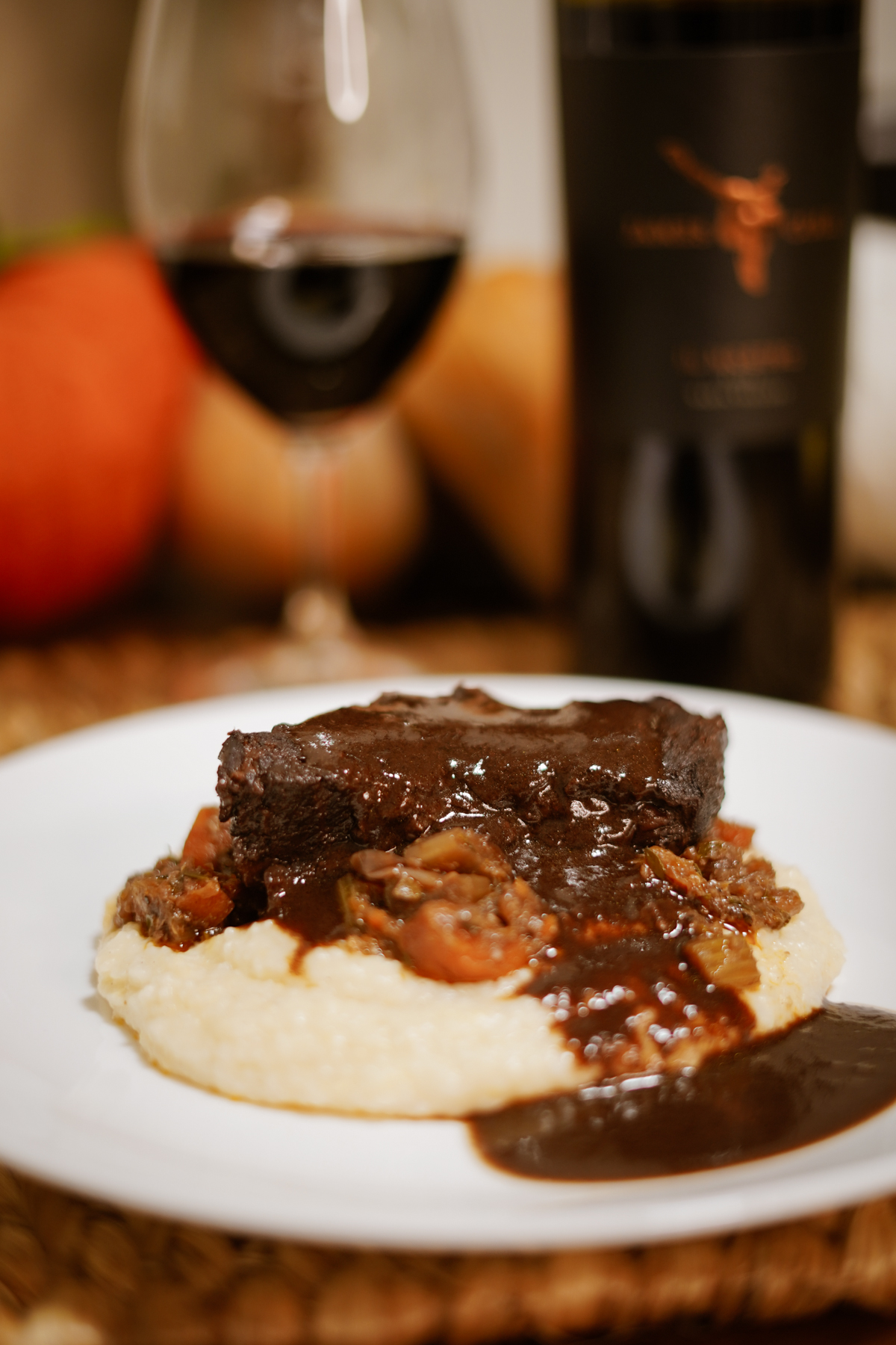 Beef Short Ribs served over Polenta on a white plate with a fall-inspired table set.