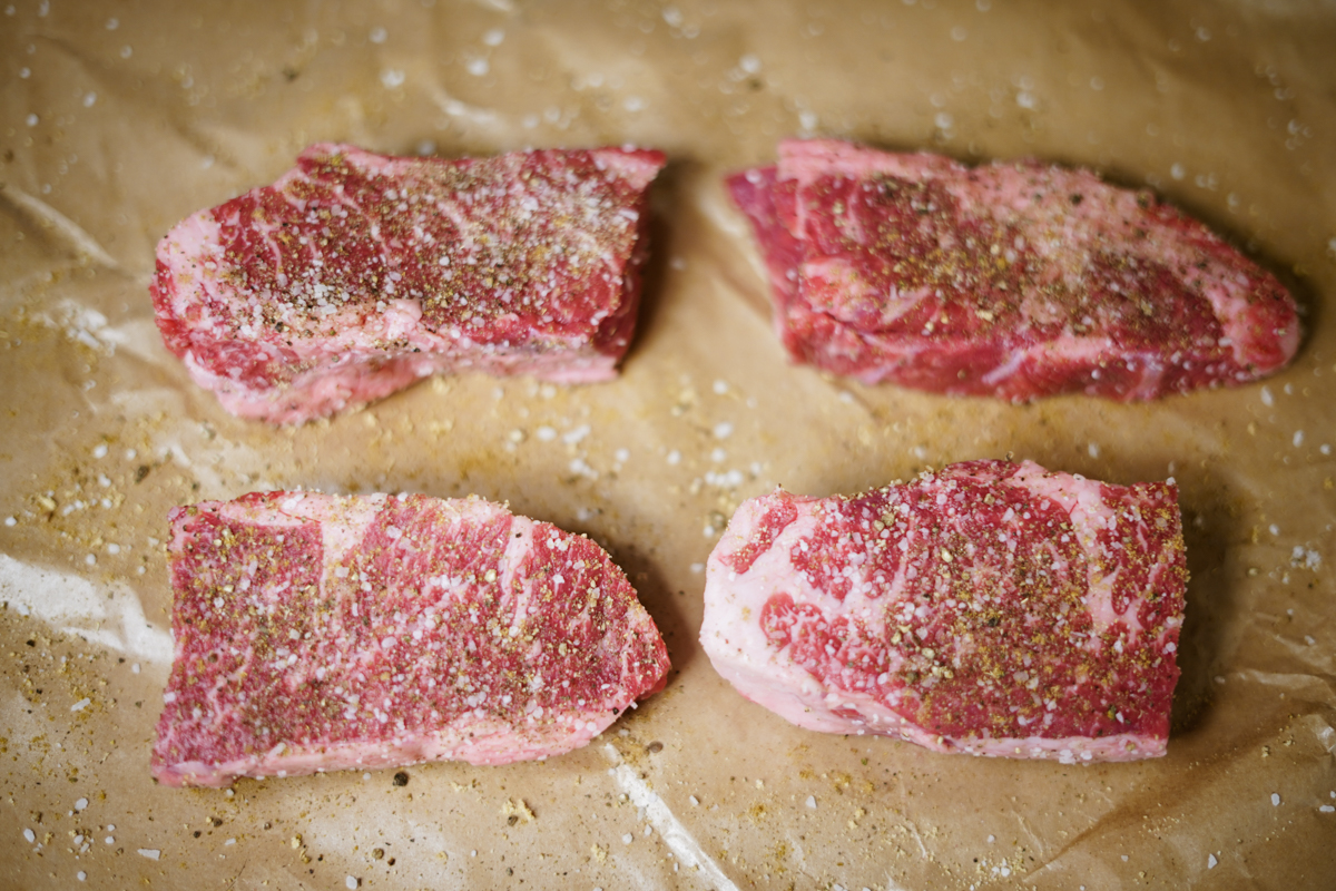 Raw beef short ribs on waxed paper with seasoning.